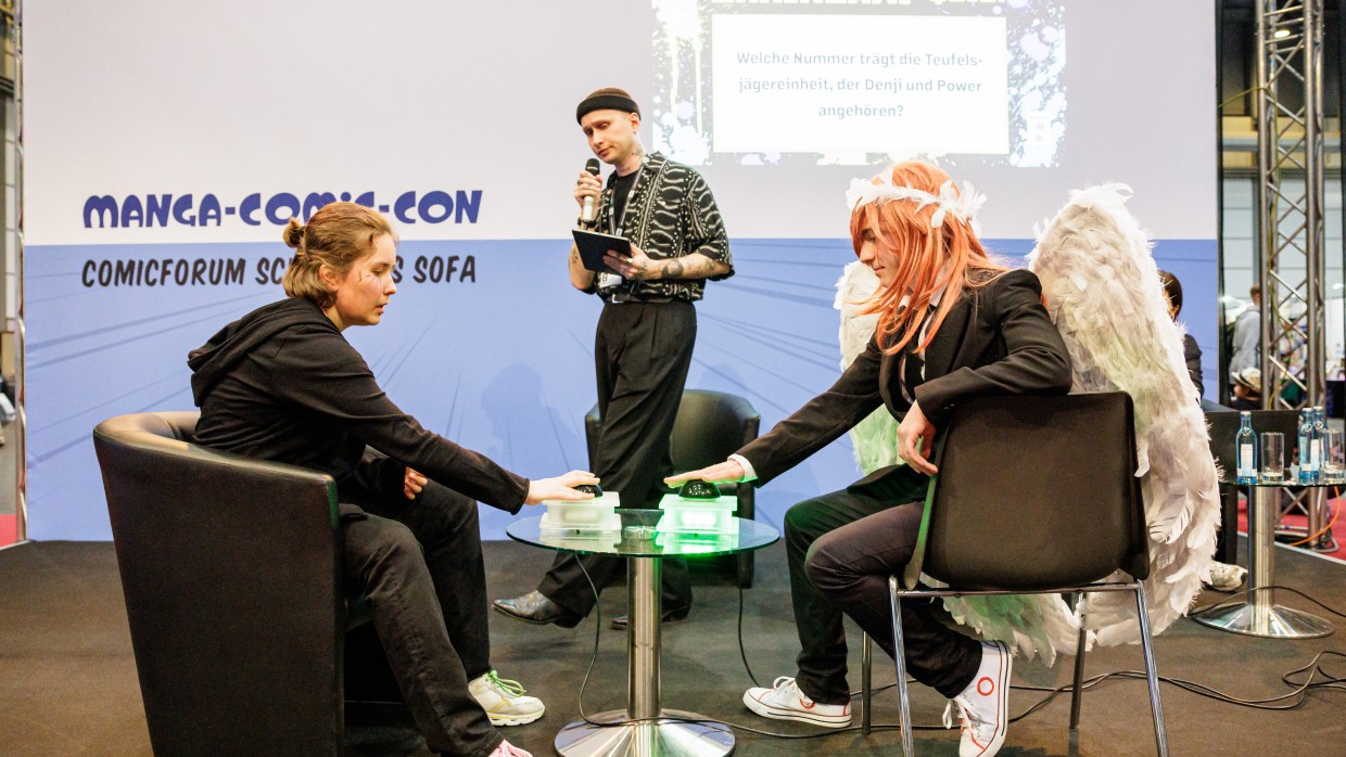 Zwei Personen sitzen auf dem Comicforum Schwarzes Sofa der Manga-Comic-Con, im Hintergrund ein Moderator.