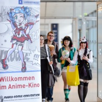 Banner des Anime Kinos auf der Manga-Comic-Con, im Hintergrund sind vier Personen zu sehen.