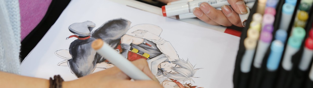 Close-up of a drawing of two manga characters being finished, with pens visible on the right.
