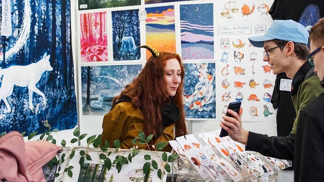 A visitor shows something on their smartphone to an exhibitor at a booth in the New Artist Alley at the Manga Comic Con 2024.
