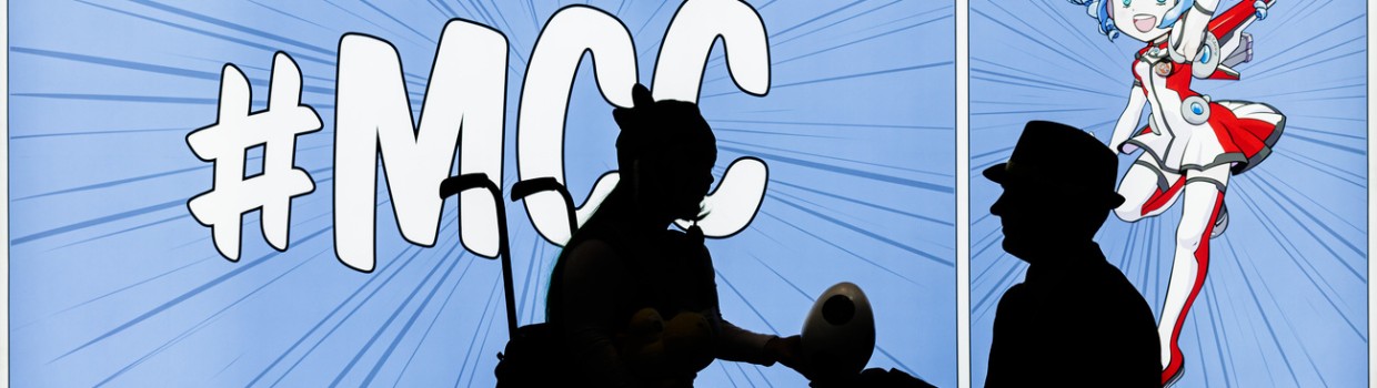 The silhouettes of two people are visible in front of a glowing wall, printed in MCC style with Macoco. One person is sitting in a wheelchair, while the other kneels in front of them, handing over an egg-shaped object