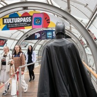 A person dressed as Batman walks through the Manga-Comic-Con, while other visitors watch with interest
