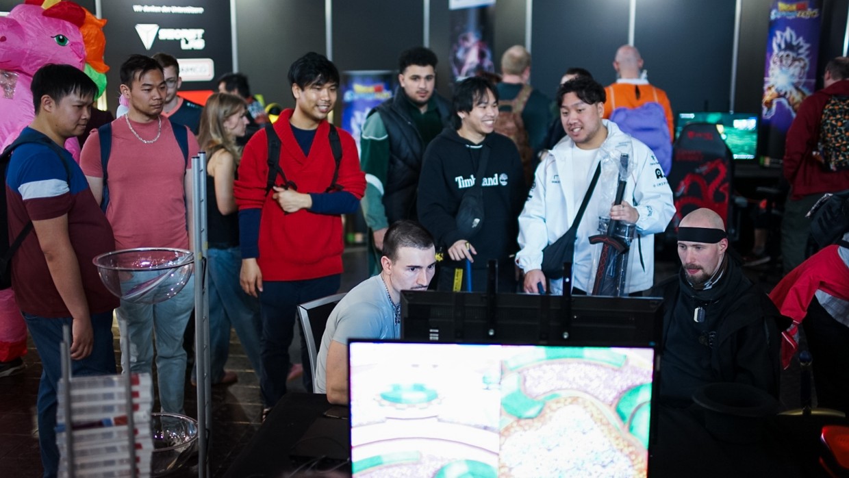 mehrere Personen sehen einem Spieler beim Computerspiel zu im Gamesroom der Manga-Comic-Con 2025
