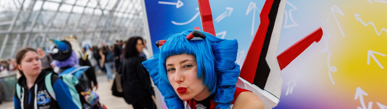 Das Maskottchen der Manga Comic Con Macoco macht einem Luftkuss vor einer bunten Leinwand auf der Manga Comic Con 2025