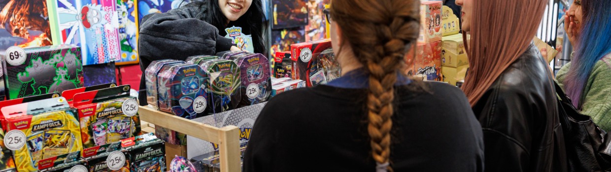 A stand with trading cards; a seller smiles at three people in front of her.
