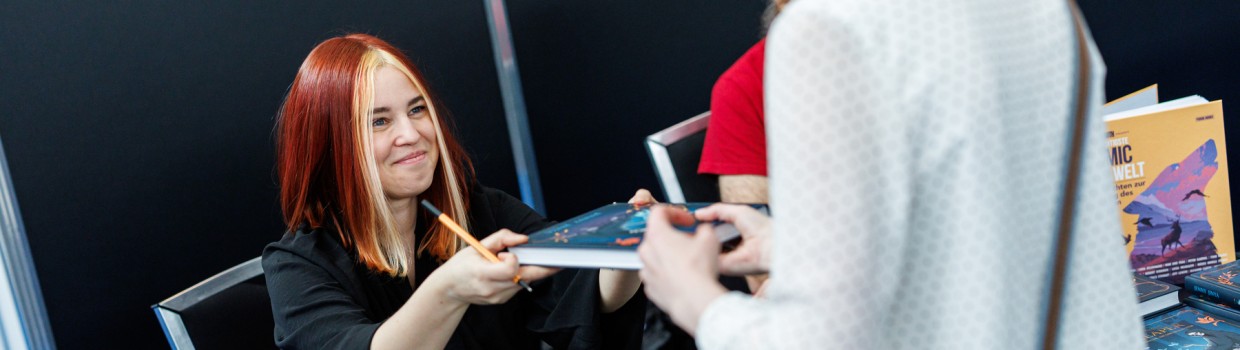 Jenny Jinya hands a fan a signed book at the Manga-Comic-Con 2025
