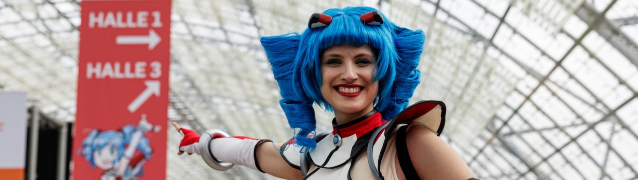 Macoco zeigt auf ein großes Banner in der Glashalle auf der Manga Comic Con 2026