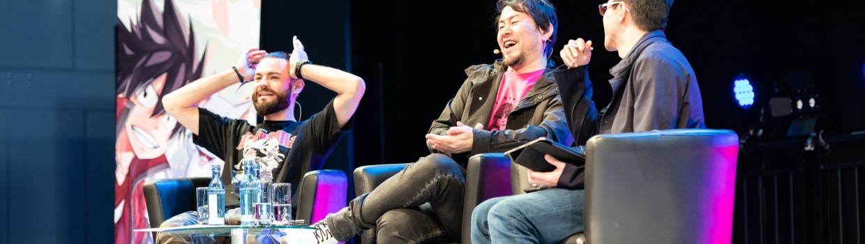 Three men are sitting next to each other on the stage and talking.
